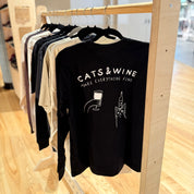 Black sweatshirt with 'Cats & Wine Make Everything Fine' text and graphics on a wooden rack.